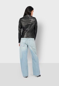 Černá kožená bunda s přiléhavým střihem, s klopovým límcem a dlouhými rukávy, v kombinaci se světle modrými kalhotami s širokými nohavicemi, které mají zadní kapsy.