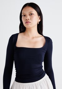 Haut à manches longues bleu marine avec un col carré, texture ajustée, tissu doux et finition lisse, associé à une jupe légère texturée.