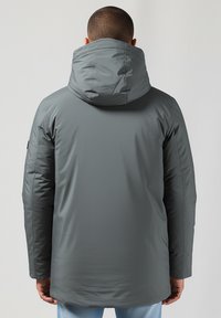 Pilkas gobtuvas su lygia, matinė paviršiumi, turintis laisvą kirpimą, ilgomis rankovėmis ir šiek tiek ilgesniu nugaros kraštu.