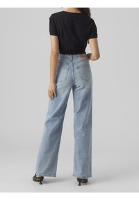 Jeans bleu clair taille haute avec une coupe droite, dotés de poches arrière et d'une texture légèrement usée, associés à un haut noir crop top.