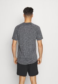 Gray sports t-shirt with a textured finish, short sleeves, and a rounded hem. Worn with black shorts, viewed from the back.