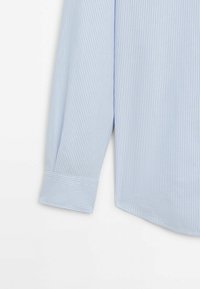 Poignet et bas de manche d'une chemise à manches longues rayée verticalement bleu clair et blanc sur fond blanc.