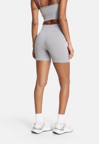 Siva športna srajca in usklajene kratke hlače iz elastičnega materiala. Kratke hlače imajo prilega obliko z elastiko. Vidna tekstura in podrobnosti tkanine.