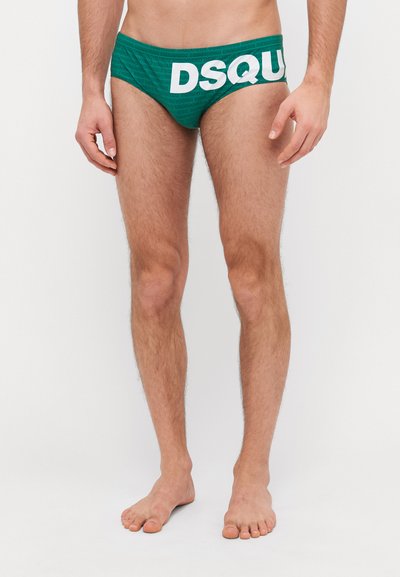Grüne Schwimmslips mit weißem "DSQUARED2"-Logo und wiederholtem Textmuster. Das Material scheint dehnbar zu sein; das Design verfügt über einen niedrigen Schnitt.