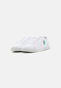 Tenisi albi din pânză cu logo verde, design cu șireturi, laturi texturate și talpă din cauciuc cu mici striații pentru aderență.