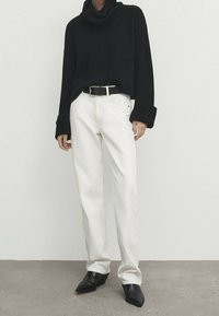 Black ribbed turtleneck sweater, white straight-leg pants, black belt, and pointed-toe black ankle boots. Smooth textures, neutral palette.
