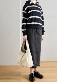 Sudadera con capucha a rayas navy y crema, diseño cropped, combinada con falda de mezclilla negra. Bolso hobo de cuero blanco, mocasines negros, detalle de dobladillo deshilachado.