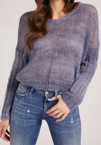 Maglione in maglia viola chiaro con vestibilità ampia, scollatura a V e maniche lunghe. Abbinato a jeans blu strappati, che mostrano un look rilassato.