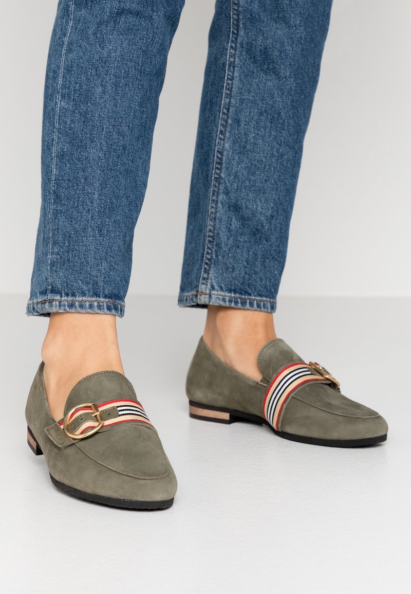 Mocassins en daim vert olive avec un bout arrondi, dotés d'un accent en boucle dorée et d'une bande rayée rouge, blanche et bleue sur le devant.