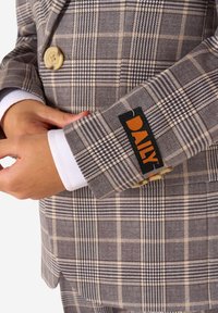 Blazer a quadri con motivi beige, marroni e neri. Presenta un bottone chiaro e un'etichetta arancione a contrasto sul polsino.