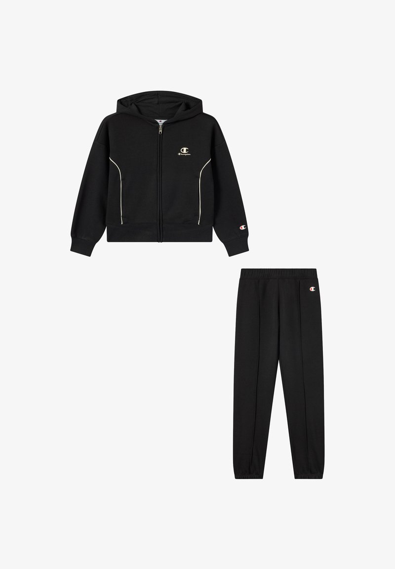 Felpa nera con zip e piping bianco, abbinata a pantaloni della tuta neri con vita elastica e dettagli con logo.