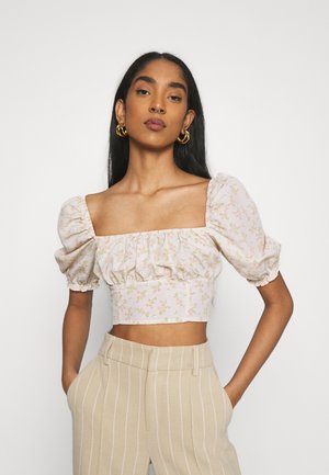 Top recortado em tecido rosa claro com estampado floral, mangas bufantes e bainha elástica. Combinado com calças de cintura alta em tons de bege com riscas.