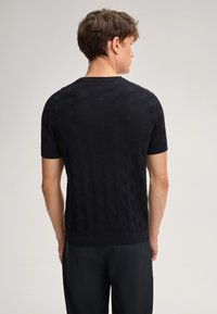 Maglione corto a maniche corte di colore nero, realizzato in maglia con una texture esagonale, colletto girocollo e orlo a coste. Modello mostrato da dietro, abbinato a pantaloni scuri.