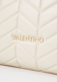 Tűzött bézs bőr kézitáska arany "VALENTINO" logóval. Figyelemre méltó chevron minta és sima felület.