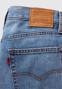 Gros plan sur la poche arrière d'un jean en denim bleu avec des coutures orange et un patch en cuir marron de la marque Levi Strauss & Co. au-dessus de la poche.