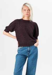 Burgundy knitted sweater with short puff sleeves and a ribbed neckline, paired with high-waisted blue jeans, featuring a relaxed fit.