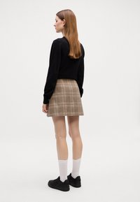 Felpa nera, mini gonna a quadri marrone, sneaker nere, calzini bianchi alla caviglia. Tessuto liscio, design casual, estetica minimalista.