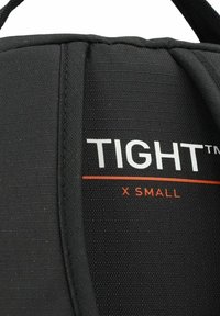 Tejido negro ajustado, con material texturizado. Etiqueta blanca "TIGHT™" y detalle naranja "X SMALL". Diseño limpio y funcional sin acentos adicionales.