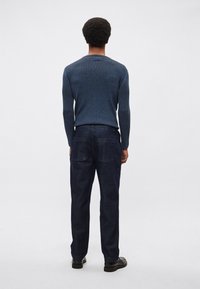 Námornícky rebrovaný pletený sveter s dlhými rukávmi, skombinovaný s tmavými džínsovými nohavicami s dvoma zadnými vreckami, oba doplnené čiernymi topánkami.