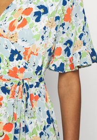 Blomstrande klänning i ljusblått med oranga, gröna och marinblå mönster. Har en omlottdesign, korta utsvängda ärmar och en knytvariant i midjan.