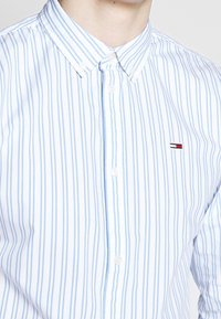 Camicia button-up a righe blu chiaro e bianche, realizzata in cotone, con un piccolo logo ricamato sul petto e un design del collo classico.