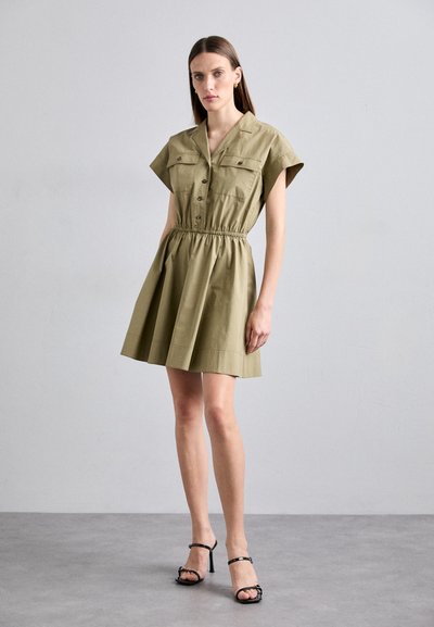 Khakifarbenes Hemdkleid mit kurzen Ärmeln, Knopfverschluss, zwei Brusttaschen, elastischem Bund und ausgestellt Rock. Getragen mit schwarzen High-Heel-Sandalen.