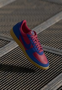 Nike sneakers med et iøjnefaldende design i pink og blå syntetiske materialer, teksturerede overflader og en gul gummisål. Klassisk snøredesign.