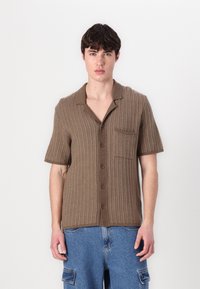 Cămașă scurtă, de culoare brună, cu mânecă scurtă, având un model texturat și rigat, cu trei nasturi și un buzunar pe piept. Se potrivește lejer și are guler.