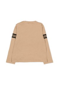 Długi rękaw beżowej koszuli wykonanej z bawełny, z czarnymi paskami na lewym rękawie, z zaokrąglonym dekoltem i subtelnymi detalami szwów.