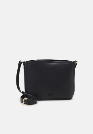 Sac bandoulière en cuir noir avec sangle réglable et petit logo embossé à l’avant sur un fond clair uni.