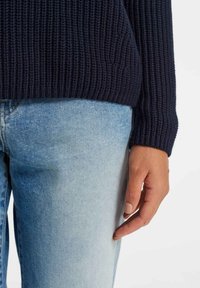 Granatowy sweter z dzianiny o prążkowanej fakturze i długich rękawach, połączony z jasnoniebieskimi dżinsami o prostych nogawkach i subtelnym spraniu.