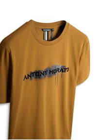 Smeđi kratki rukavi majica od mekog materijala s crnim grafičkim printom u stilu spreja i natpisom "ANTONY MORATO" na prednjoj strani.