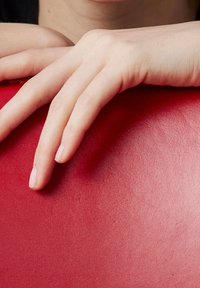 Deux mains pâles reposant doucement sur une surface rouge lisse, les doigts légèrement écartés et détendus.