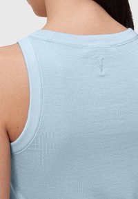 Světle modrý žebrovaný top bez rukávů s kulatým výstřihem, se subtilním logem vyšitým na zadní straně a hladce dokončenými okraji.