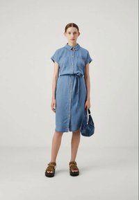 Jeanskjole med krage, korte ermer, knappelukking foran og belte i livet, supplert med beige platåsandaler og en blå håndveske.