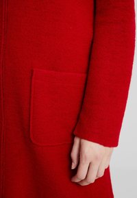 Röd ullrock med en mjuk textur, långa ärmar och en framficka med en ren design och minimalt synliga sömmar.