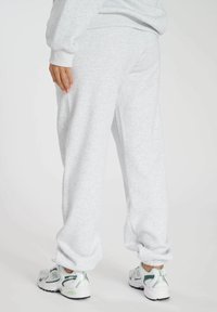 Hellgraue Sweatpants aus weichem Material, mit lockerer Passform und gerippten Bündchen an den Knöcheln, kombiniert mit weißen und grünen Sportschuhen.