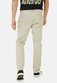 Beige bukser med slim fit og lige ben. Har baglommer med knaplukninger. Bæres med en sort t-shirt og casual sko.