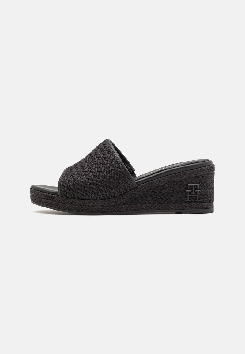 Sandale à talon compensé noire avec un dessus tissé, un design à bout ouvert, une surface texturée et un logo en relief sur le talon.
