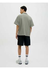 Camiseta gris de manga corta acanalada combinada con pantalones cortos de cargo negros, calcetines blancos con rayas negras y zapatillas deportivas grises. Diseño sencillo y moderno.