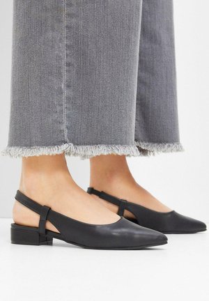 Ballerine slingback in pelle nera con punta affusolata, tacco a blocco basso e schienale aperto, abbinate a jeans grigi cropped con orlo sfrangiato.