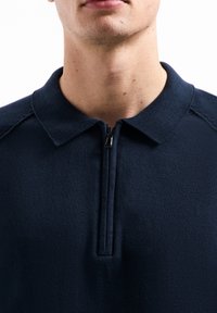 Marineblauwe poloshirt met een ritssluiting aan de hals, gemaakt van getextureerde stof. Kenmerkt zich door een klassieke kraag en een naadloos schouderontwerp voor comfort.