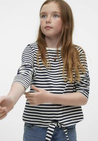 Maglia a maniche lunghe a righe in navy e bianco, con hem annodato e maniche arrotolate, abbinata a pantaloni corti in denim.