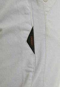 Lichtgrijze stof met een gladde textuur, voorzien van een zwart accentpatch en oranje "CHASIN'" branding. Gedetailleerde stiksels langs de naden.