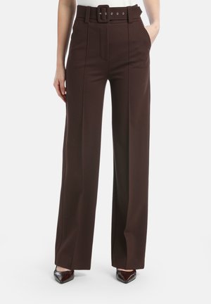 Høj talje, mørkebrune, vidde benbukser med forstykker foran og matchende bælte med en rektangulær spænde, båret med mørke spidse sko.