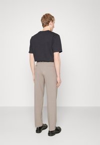 Maglietta nera a maniche corte abbinata a pantaloni beige a gamba dritta, che completano delle scarpe in pelle nera. Design semplice e pulito senza motivi visibili.