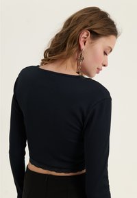 Navy ribbed pitkähihainen crop-top, jonka helman reunassa on pitsiä, pyöreä pääntie ja kapea muotoilu, yhdistettynä mustiin korkea vyötäröisiin housuihin.