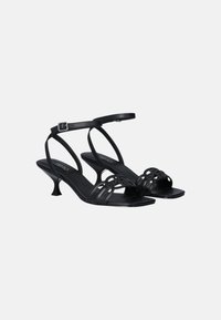 Sandali neri in pelle con tacco alto, cinturini incrociati, fibbia alla caviglia e tacco appuntito scolpito. Superficie liscia e design minimalista.