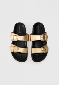 Χρυσές μεταλλικές σανδάλες με δύο ρυθμιζόμενες αγκράφες, μαύρη σόλα και λεία επιφάνεια. Ελαφρύς σχεδιασμός για άνεση.
