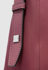 Burgunderfarbene Handtasche mit glatter Textur, ausgestattet mit einem Lederhenkel und einem silbernen Metallakzent. Die Oberfläche weist feine Nähte auf.